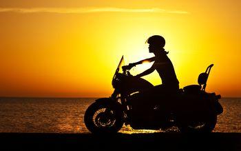 Motocyklistka na motorze na tle zachodzącego słońca