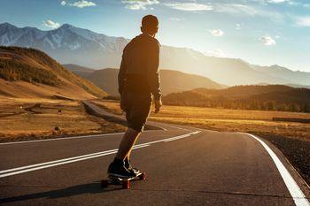 Chłopak zjeżdżający na longboardzie na tle gór