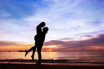 Przytulająca się para na plaży na tle zachodzące słońca