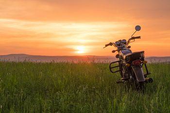  Motocykl zaparkowany na trawie na tle zachodzącego słońca